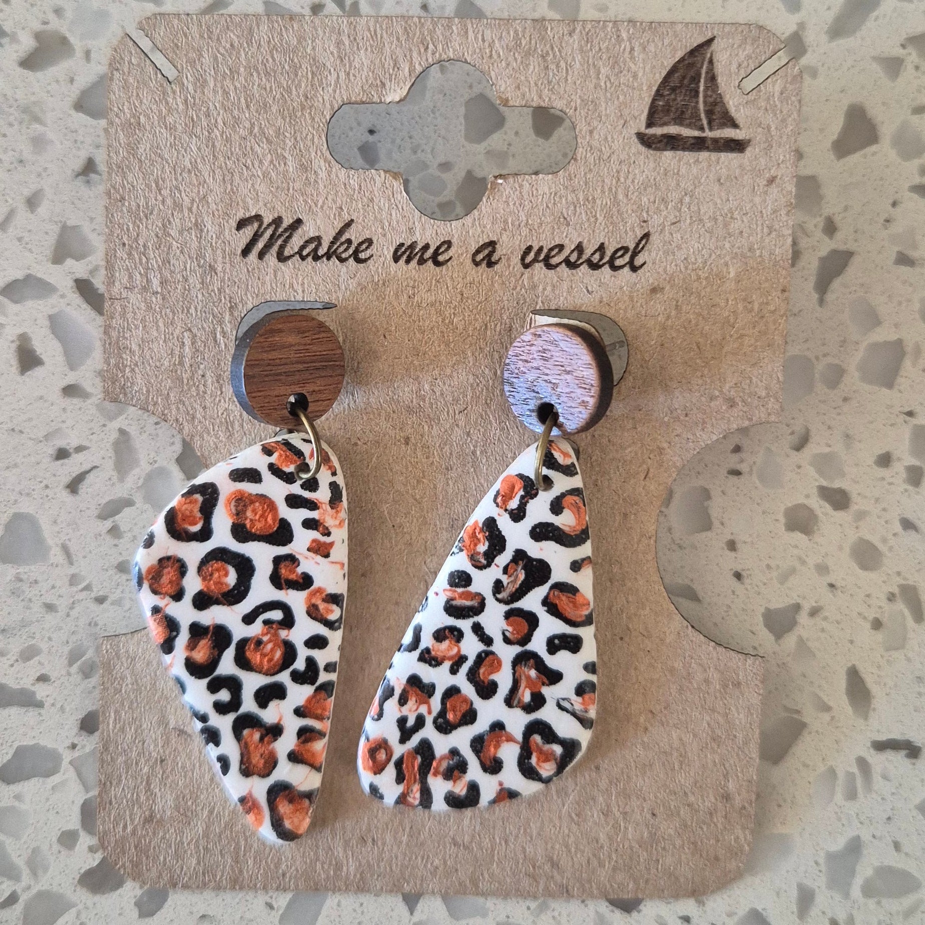 Leopard print earrings on a branded card with a textured surface background