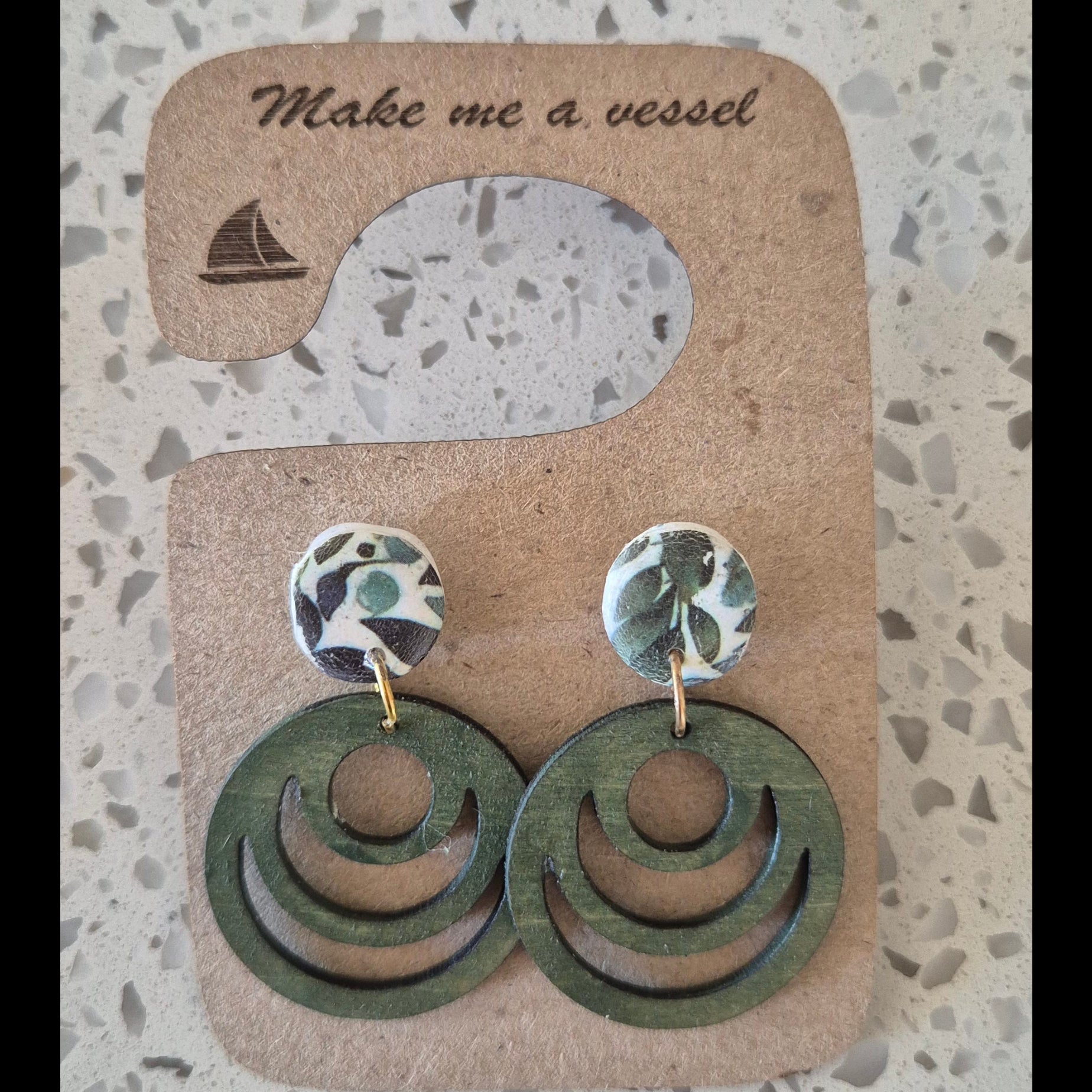 Green circular earrings on a branded card with 'Make a Vessel' text on a textured surface.