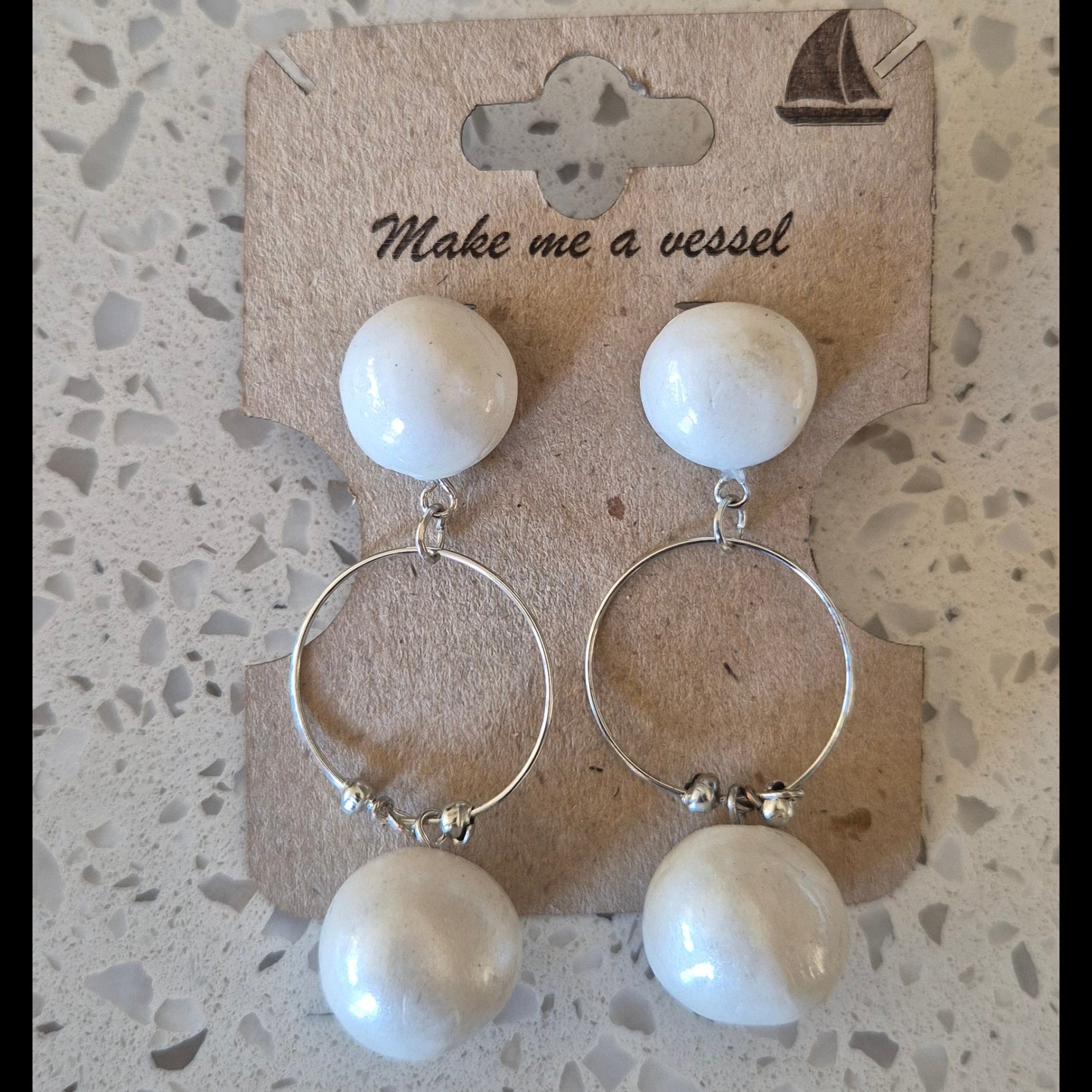 Set of earrings on a display card with 'Make me a vessel' text on a textured surface.