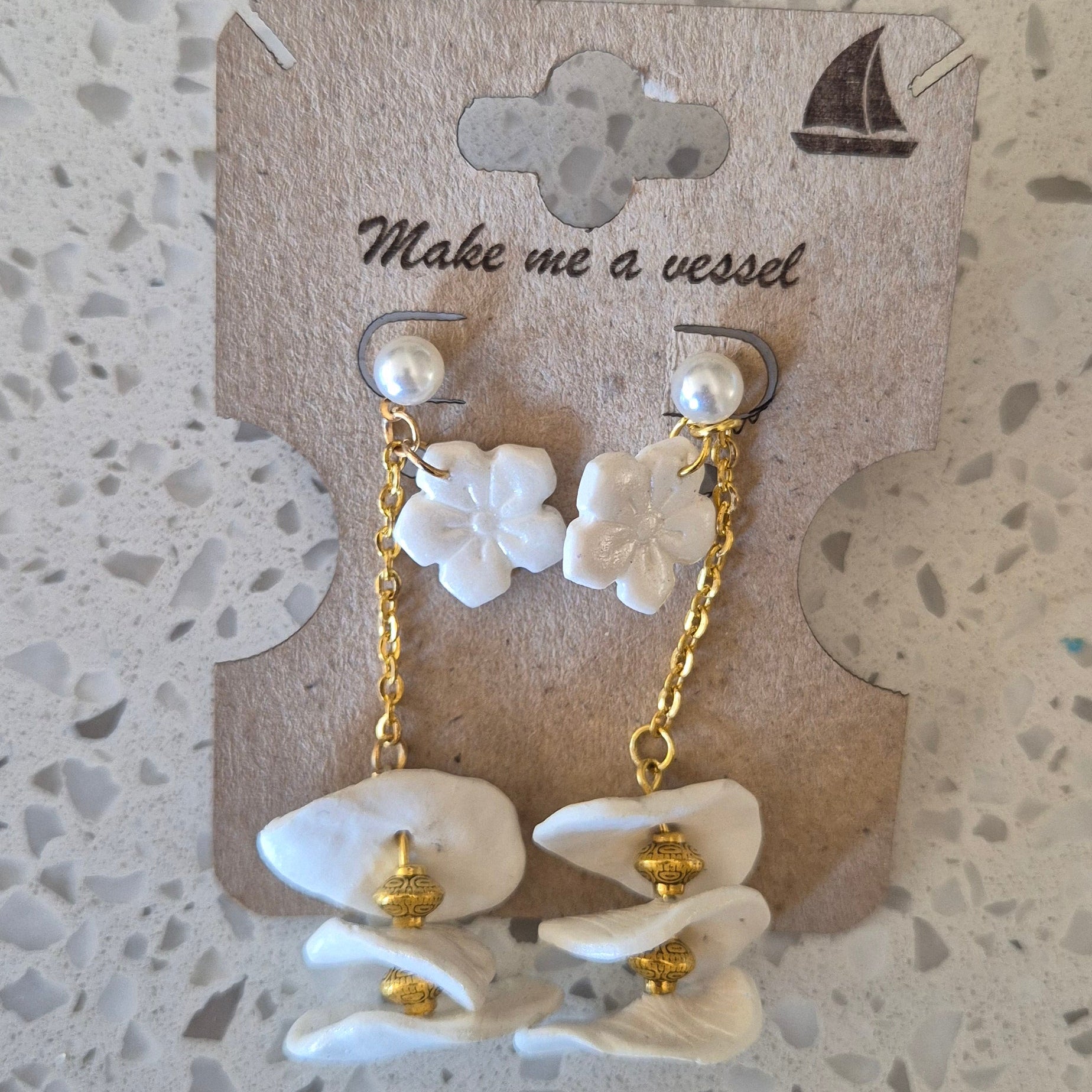 Pair of white floral earrings with gold accents on a branded card. Wedding range.