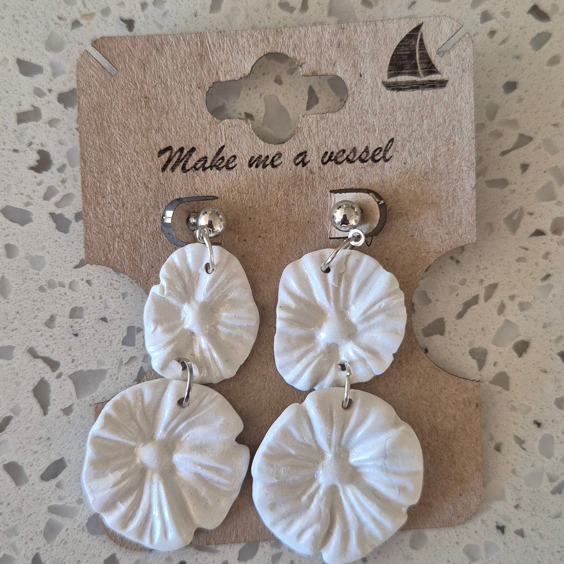 White floral earrings on a branded card with a textured surface background