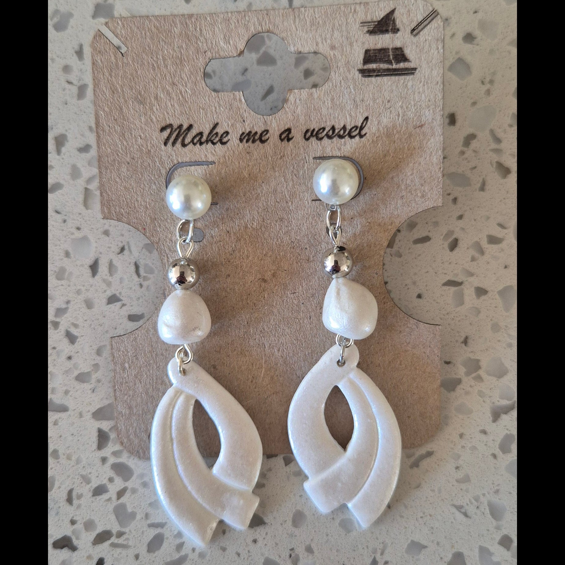 Pair of white earrings on a branded card against a textured surface